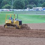Tractor pushing dirt on an athletic field.
